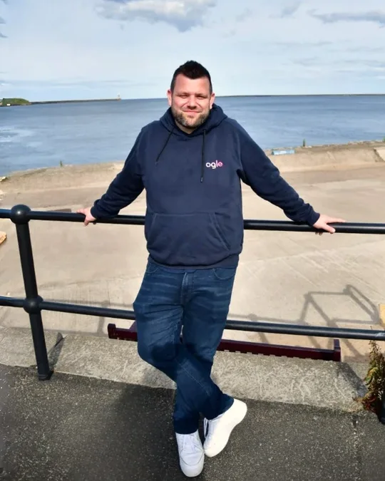 Chris Ogle in an Ogle hoodie, leaning on the railings at the coast